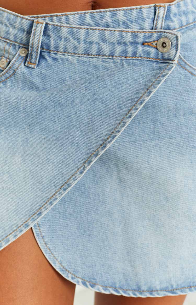 Close-up of the light blue faded denim asymmetrical wrap mini skirt with a button closure