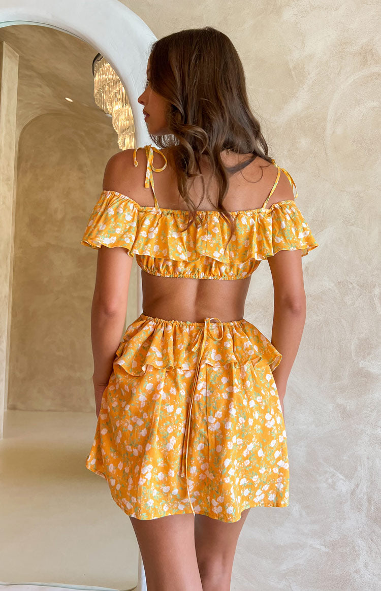 Rear view of an orange floral mini dress with off-shoulder ruffles, tie straps, and a cutout elasticated waist