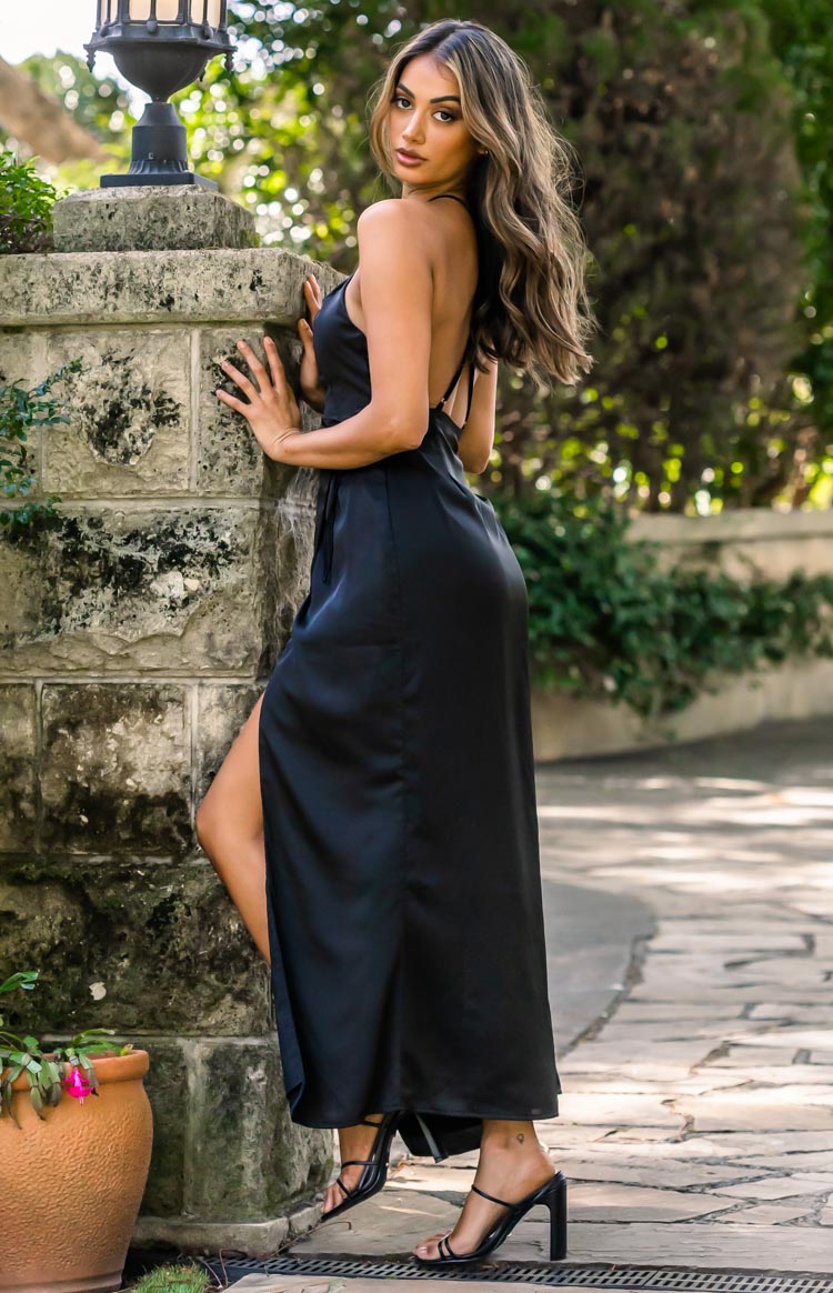 Side view of a black satin maxi dress with a low scoop back, thin cross-back straps, and a high side slit