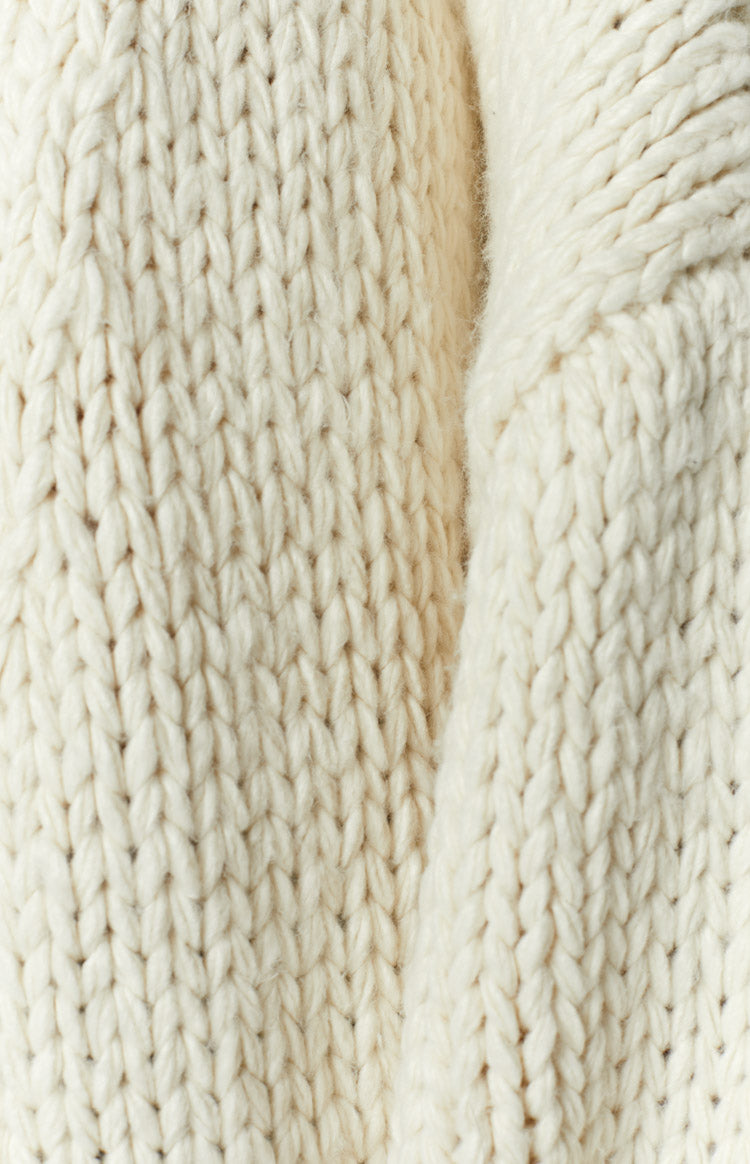 Close-up of the cream chunky knit fabric with thick, visible stitches and a soft, plush texture