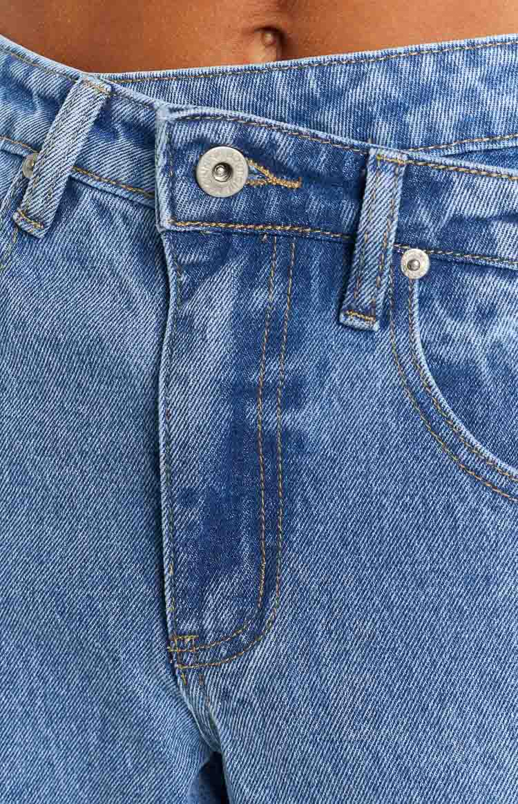 Close-up of the button fly closure and front pocket detail on blue denim jeans