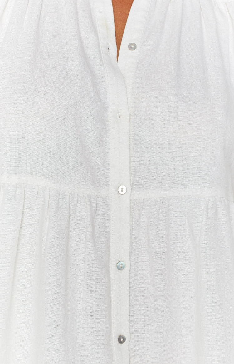 Close-up of the white linen dress showing the button-front placket with iridescent shell buttons and gathered bodice