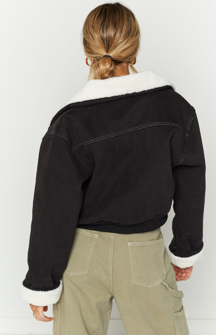 Rear view of a black denim sherpa jacket with a wide white sherpa collar, rolled cuffs showing white sherpa, and white contra