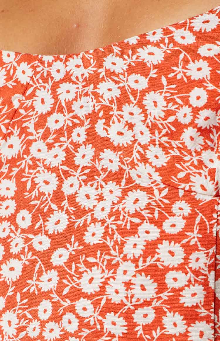 Close-up of the orange midi dress fabric featuring a white small daisy floral pattern with delicate leaves