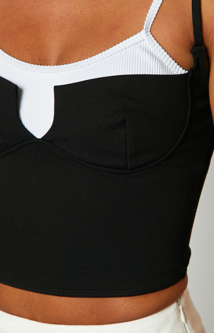 Close-up of the black crop top's V-cutout neckline and bust seam detail over a white ribbed underlayer