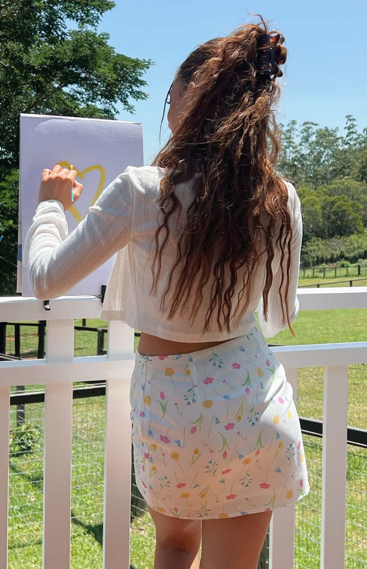 Side and back view of a white mini skirt with a scattered floral print in pink yellow and blue