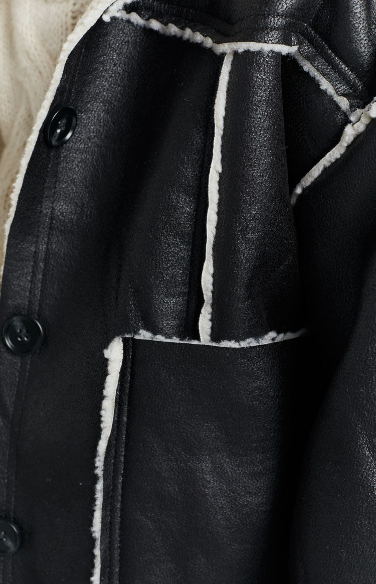 Close-up of the black faux leather jacket showing its texture, white fur trim along the seams, and a black button