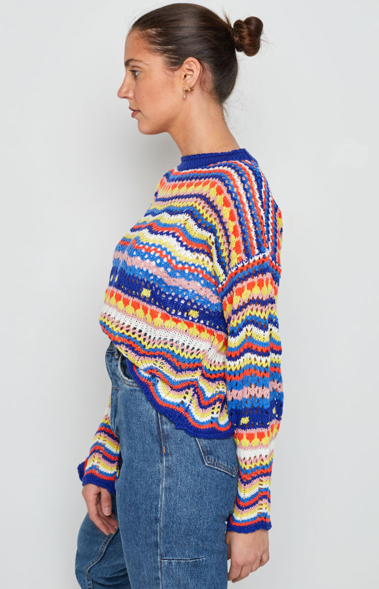 Open-knit sweater with vibrant multi-coloured stripes, blue ribbed crew neck and cuffs
