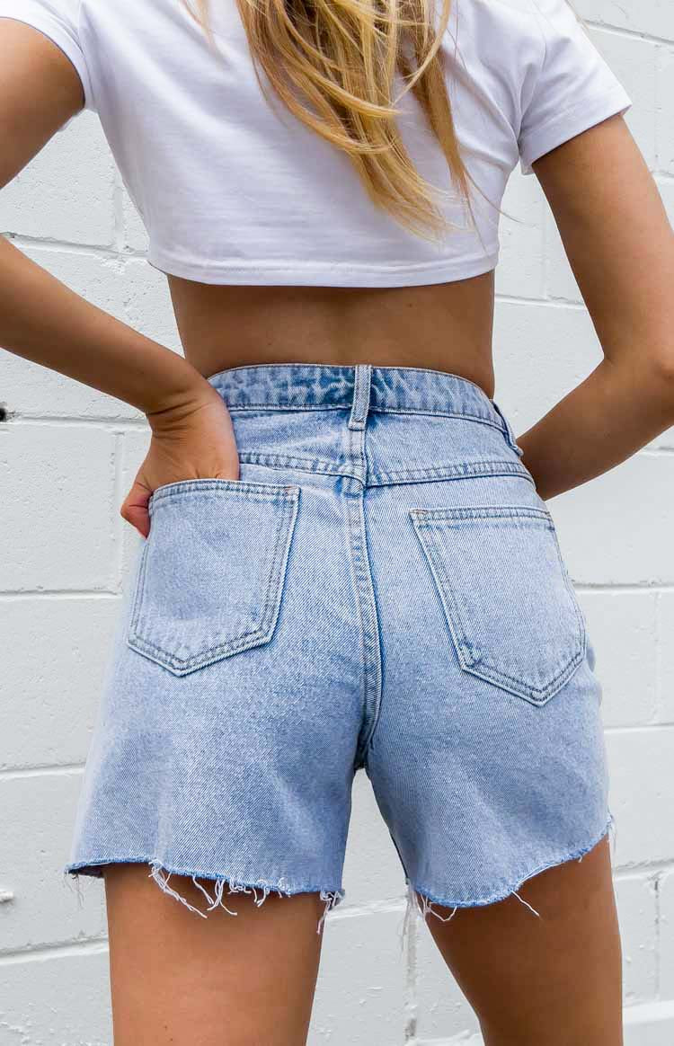 Rear view of light blue denim shorts with back pockets and distressed raw hems