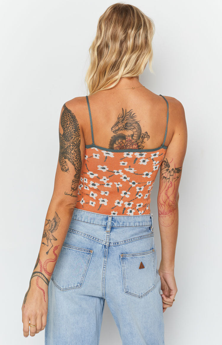 Fitted orange knit crop top with white blossom pattern, thin green straps, and green trim at back