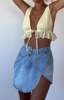 Light wash denim asymmetrical wrap mini skirt with a visible button closure and side pocket